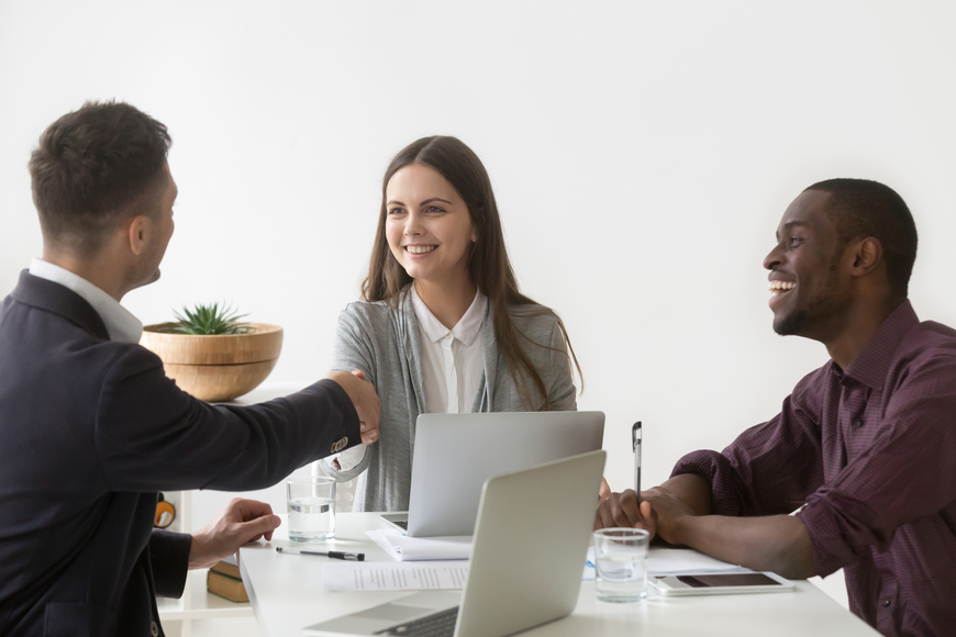 Smiling businesswoman shaking hand of male partner at group meet